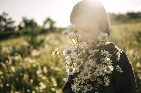 Boy holding bunch of daisies in field - ANAF01731