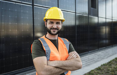 Lächelnder Ingenieur mit verschränkten Armen vor einem Solarpanel - UUF29337