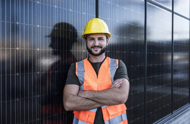 Lächelnder Ingenieur, der sich mit verschränkten Armen über Solarzellen lehnt - UUF29340