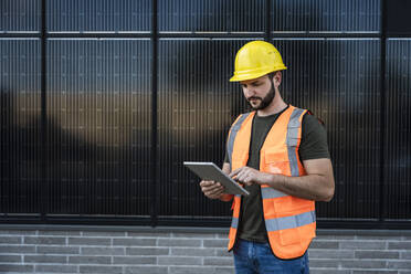 Engineer using tablet PC standing in front of solar panels - UUF29341