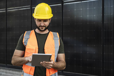 Engineer working on tablet PC in front of solar panels - UUF29342