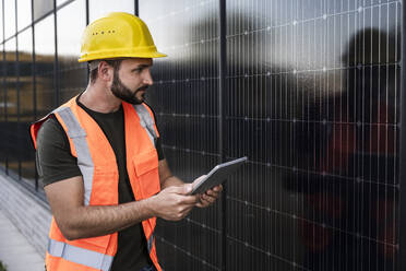 Engineer holding tablet PC and looking at solar panels - UUF29351