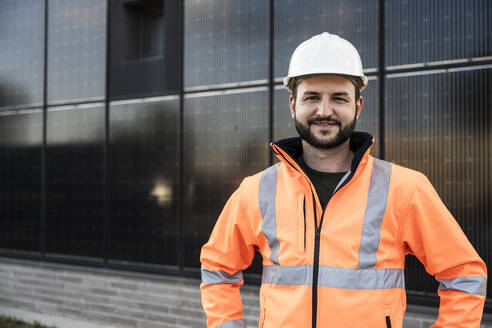 Ein lächelnder, selbstbewusster Ingenieur steht vor einem Solarpanel - UUF29354