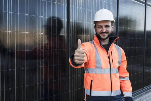 Lächelnder Ingenieur, der in der Nähe von Solarmodulen den Daumen hoch streckt - UUF29358