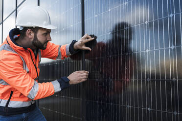 Ingenieur bei der Arbeit in der Nähe einer Wand mit Solarzellen - UUF29361