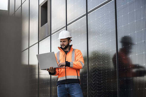 Engineer working through laptop standing near solar panels - UUF29364