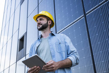 Contemplative engineer holding tablet PC in front of solar panels - UUF29388