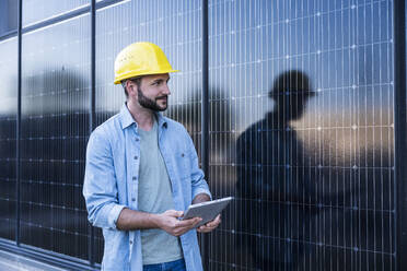 Ingenieur in Jeanshemd und mit Tablet-PC in der Nähe von Solarzellen - UUF29389