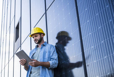 Engineer using tablet PC leaning on solar panels - UUF29392