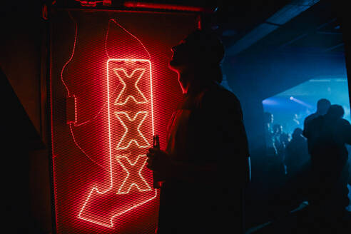 Side view silhouette of unrecognizable man in street style outfit standing in night club near neon sign - ADSF44918