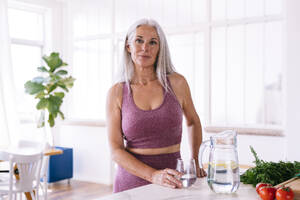 Lächelnde Frau mit einem Glas Wasser an der Küchentheke zu Hause - OIPF03223