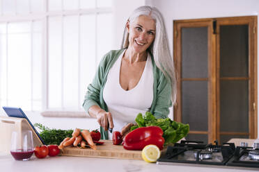 Smiling woman cutting tomato with knife at home - OIPF03237