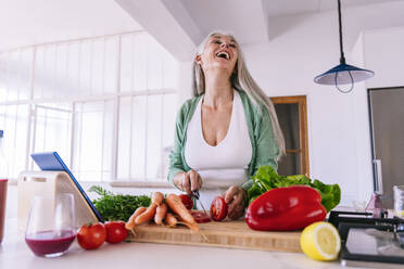 Fröhliche Frau, die zu Hause eine Tomate mit einem Messer schneidet - OIPF03238