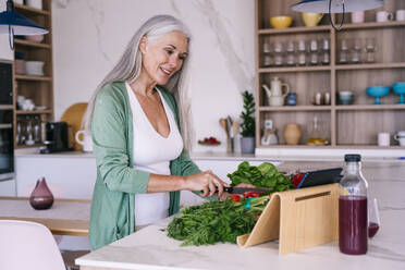 Smiling mature woman watching tutorial and preparing food at home - OIPF03242
