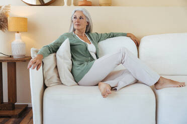 Nachdenkliche Frau sitzt zu Hause auf dem Sofa - OIPF03251