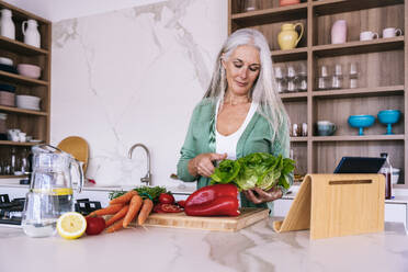 Lächelnde reife Frau mit Gemüse bei der Zubereitung von Essen zu Hause - OIPF03268