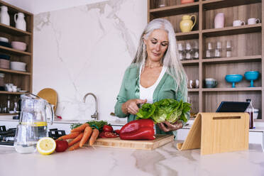 Smiling mature woman with vegetables preparing food at home - OIPF03268