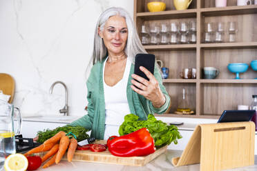 Smiling mature woman talking on video call in kitchen at home - OIPF03272