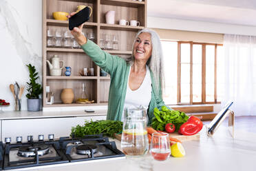Ältere Dame fängt einen freudigen Moment in ihrer Küche ein, indem sie ein Selfie in ihrer gemütlichen Wohnung macht - OIPF03273