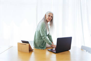 Älterer Freiberufler sitzt mit Laptop auf dem Tisch zu Hause - OIPF03276