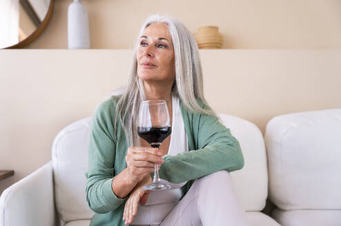 Nachdenkliche Frau mit einem Glas Wein auf dem Sofa zu Hause - OIPF03289