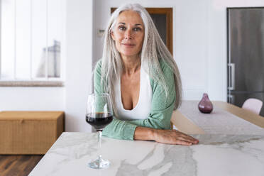 Lächelnde Frau mit einem Glas Wein an einer Kücheninsel lehnend - OIPF03291