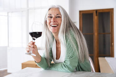 Happy woman with glass of wine leaning on kitchen island - OIPF03292