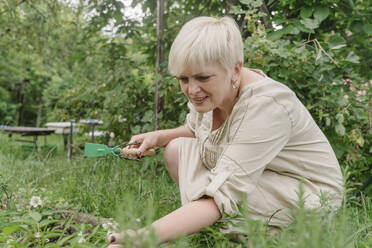 Mature woman crouching on grass in garden - OSF01835