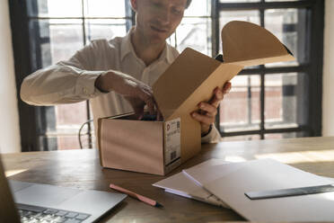 Geschäftsmann beim Auspacken eines Pakets am Schreibtisch - VPIF08302