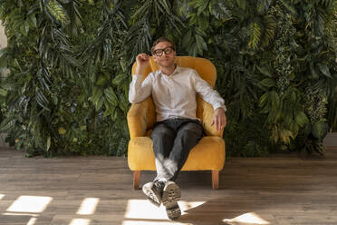 Smiling businessman sitting in yellow armchair - VPIF08316