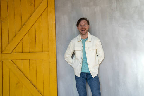 Happy mature man leaning on gray wall at home - VPIF08324