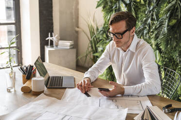 Mature businessman with blueprints at desk - VPIF08340