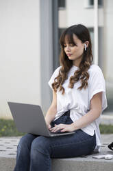 Student using laptop in front of building - LMCF00338