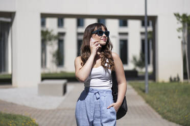 Junge Frau mit Sonnenbrille, die mit einem Smartphone telefoniert - LMCF00349