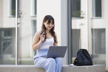 Lächelnde junge Frau winkt bei einem Videogespräch über einen Laptop - LMCF00350