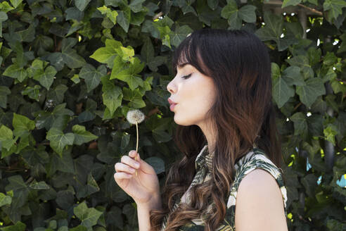 Young woman blowing on dandelion flower - LMCF00358