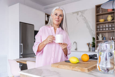Reife Frau stehend mit Kaffeetasse in der Küche zu Hause - OIPF03307