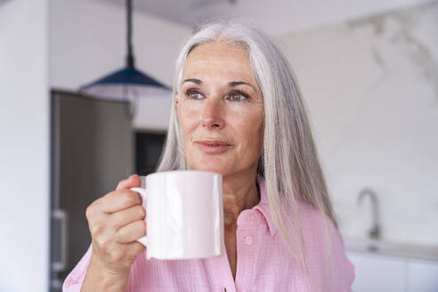 Contemplative mature woman holding coffee cup at home - OIPF03308