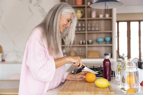 Smiling woman cutting orange using knife at home - OIPF03311