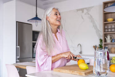 Happy mature woman cutting fruit in kitchen at home - OIPF03313