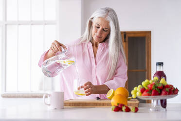 Mature woman pouring detox water in glass at home - OIPF03316