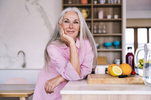 Lächelnde Frau lehnt sich zu Hause an die Küchentheke - OIPF03337
