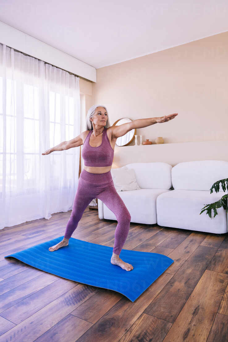 Woman exercising with arms outstretched on yoga mat at home stock photo