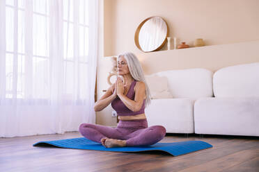 Mature woman meditating in living room at home - OIPF03383