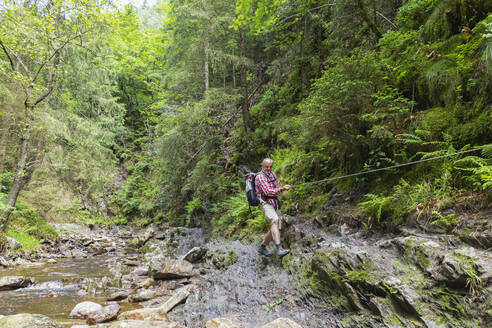 Älterer Mann beim Wandern mit Seil im Wald - GWF07861