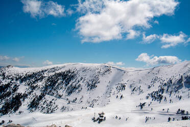 Picturesque view of snowy mountain range covered with snow against cloudy blue sky during winter season in countryside - ADSF45002