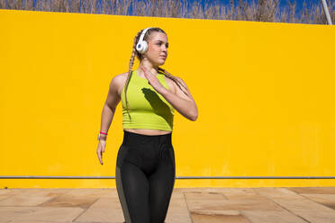 Confident young fit female athlete in sportswear running fast while looking away near yellow wall in daylight - ADSF45025