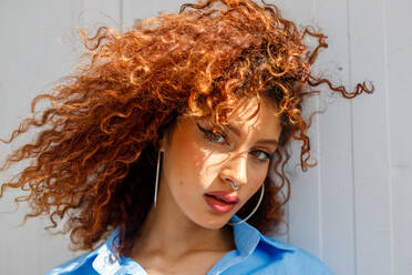 Portrait of a young model with curly red hair and nose piercing looking seductively at the camera from the side - ADSF45032