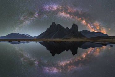 Picturesque landscape of Krossanesfjall mountain ridge under colorful bright sky with Milky Way reflecting in pond at night in Iceland - ADSF45051