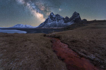 Picturesque scenery of rocky Krossanesfjall mountain range with uneven surface located near calm pond under blue sky with stars in Iceland - ADSF45054